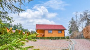 A wooden cabin with a red roof, surrounded by a paved walkway and dense greenery. - 2 bedroom awesome home in Jaroslawiec (Jaroslawiec)