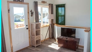 Une pièce avec une porte en bois portant l’inscription « REACH », une fenêtre avec des rideaux, une lampe, une malle en bois et une petite table.