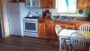 Une cuisine dotée de meubles en bois, d’un réfrigérateur, d’un four à micro-ondes, d’un four traditionnel et d’un coin repas avec une table et des chaises.