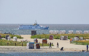 A beach with portable cabins and a boat in the background. - Cozy apartment in Büsum with WiFi (Büsum)