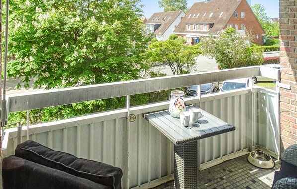 A balcony with a metal railing, a small table with a white mug, a wicker chair, and a metal dog bowl. - Cozy apartment in Büsum with WiFi (Büsum)