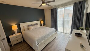 Ein Schlafzimmer mit Bett, Nachttischlampen, Deckenventilator, Fenster mit Vorhängen, Kommode und einer kleinen Pflanze.