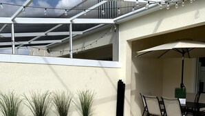 Ein Pool mit Fliesen, Blumentöpfen, Gartenmöbeln und Lichterketten.