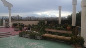 A rooftop garden with potted plants, a wooden bench, and a view of distant mountains. - Maisonnette Frond de mer (Frontignan)