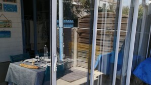 A patio area with a table set for dining, a sliding glass door leading to a covered outdoor space, and a clock on the wall. - Maisonnette Frond de mer (Frontignan)