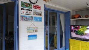 A room with a wooden wall adorned with various travel-themed posters, a yellow cabinet with a television, and a window with blue shutters. - Maisonnette Frond de mer (Frontignan)