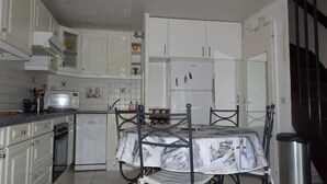 A compact kitchen with white cabinets, a small refrigerator, a microwave, and a dining table with a metal frame. - Maisonnette Frond de mer (Frontignan)