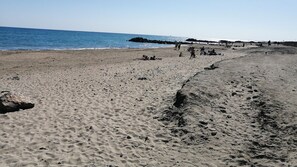 A beach with a rocky shoreline, people walking, and a pier in the background. - Maisonnette Frond de mer (Frontignan)