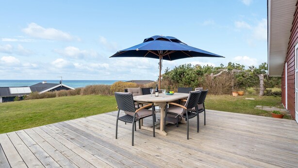 Une terrasse en bois avec une table ronde et quatre chaises, un parasol et une bouteille de vin.