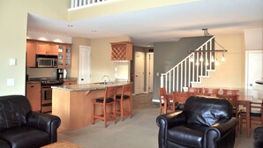 Amplia sala de estar con cocina, comedor y una escalera que lleva a un nivel superior.