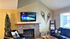 Una sala de estar con chimenea de piedra, un árbol de Navidad, muebles de cuero y un televisor de pantalla plana sobre la chimenea.