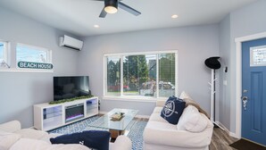 Una sala de estar con televisor, sofás blancos, una mesa de centro y un ventilador de techo.