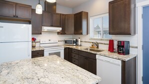 Una cocina con armarios de madera oscura, un refrigerador blanco, estufa, microondas, cafetera y lavavajillas.