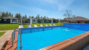 A swimming pool with a wooden deck and lounge chairs, surrounded by small houses with a green lawn and trees. - Beautiful home in Postomino (Postomino)