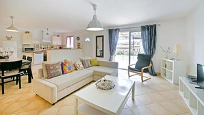 A modern living room with a sofa, coffee table, and a dining area with chairs. There is a kitchen in the background with white cabinets and a microwave. - Amazing home in Bordezac (Bordezac)