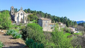 A stone church with a bell tower and a clock, surrounded by greenery and houses on a hillside. - Amazing home in Bordezac (Bordezac)