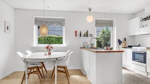 A modern kitchen with white cabinetry, a wooden dining table with chairs, a small island with a sink, and an oven. - Beautiful home in Svaneke with WiFi (Svaneke)