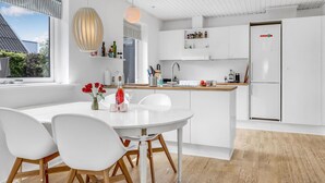 A modern kitchen with white cabinetry, a central island with seating, and a large window providing natural light. - Beautiful home in Svaneke with WiFi (Svaneke)
