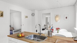 A modern kitchen with a wooden countertop, stainless steel sink, and white cabinetry. - Beautiful home in Svaneke with WiFi (Svaneke)