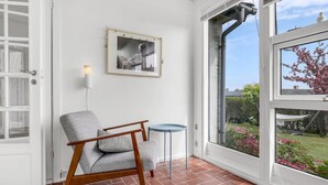 A room with a view of a garden, a chair, a small table, and a framed picture on the wall. - Beautiful home in Svaneke with WiFi (Svaneke)