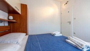 Une chambre à coucher avec un lit, une armoire en bois, une porte blanche et une couverture bleue à motifs.