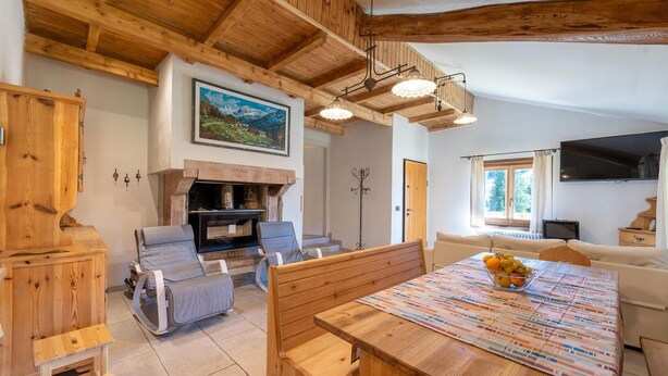 A cozy living room with a wooden ceiling, a fireplace, a dining table with a fruit bowl, and a sofa. - Beautiful home in Castello Tesino (Castello Tesino)