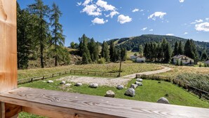 A wooden deck with a view of a rural landscape, including a fenced area with rocks, a dirt path, and houses in the background. - Beautiful home in Castello Tesino (Castello Tesino)