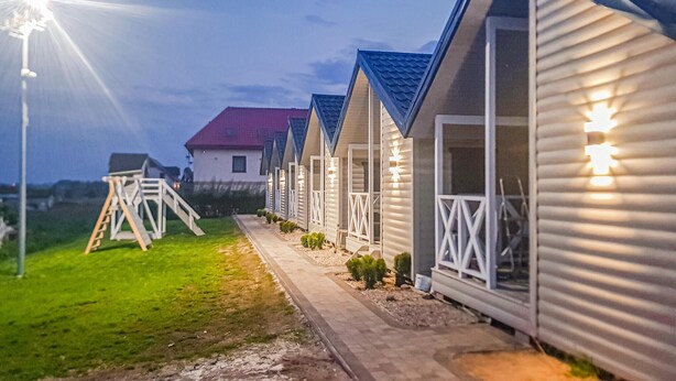 Una hilera de cabañas frente a la playa, con un camino que lleva a la entrada, cada una con un balcón y un pequeño jardín.