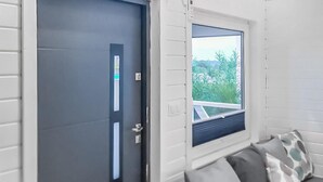 Una habitación con una puerta oscura, una ventana que da a zonas verdes y un sofá con cojines estampados.
