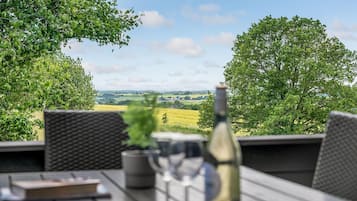 Et udendørs siddeområde med udsigt over et grønt landskab, en flaske og et glas.