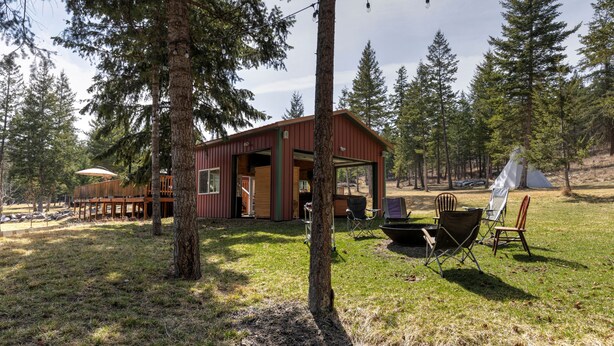 A cabin with an open door, surrounded by trees, and outdoor seating with a table and chairs. - Clear Creek Mountain Cabin With Lake Access (Polson)