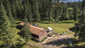 A cabin with a deck, surrounded by dense forest and a view of a lake and mountains. - Clear Creek Mountain Cabin With Lake Access (Polson)