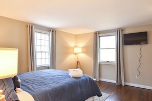 Una habitación de hotel con cama, lámpara, televisión y dos ventanas con cortinas.
