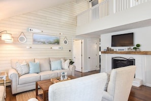 A spacious living room with a high ceiling, a fireplace, and a television mounted above it.