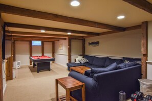 Una habitación con mesa de billar, sofá, mesa de centro de madera y una decoración de peces en la pared.