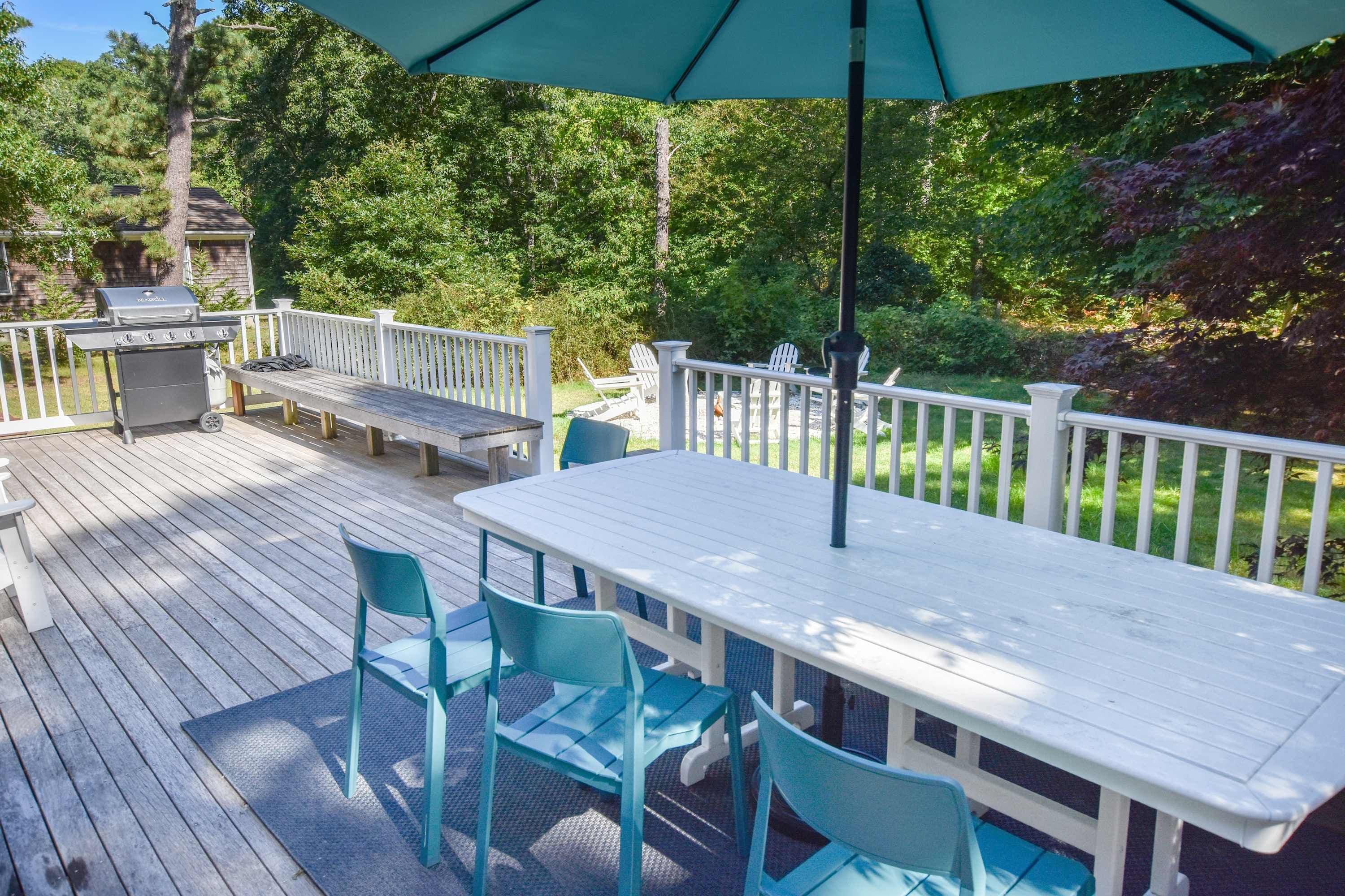 A deck with a table and chairs, a grill, and a white fence.