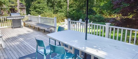 A deck with a table and chairs, a grill, and a white fence.