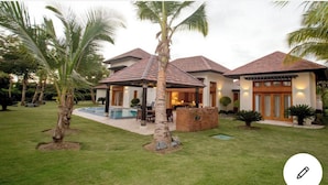 Une maison à deux étages avec une piscine, entourée de palmiers et d’une pelouse bien entretenue.