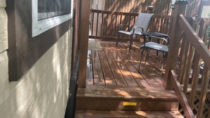 Una terraza de madera con barandilla metálica, un banco y una silla.