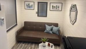 Una habitación acogedora con un sofá marrón, dos cuadros enmarcados con imágenes de cactus, una mesita con una planta y un mueble negro para televisor.