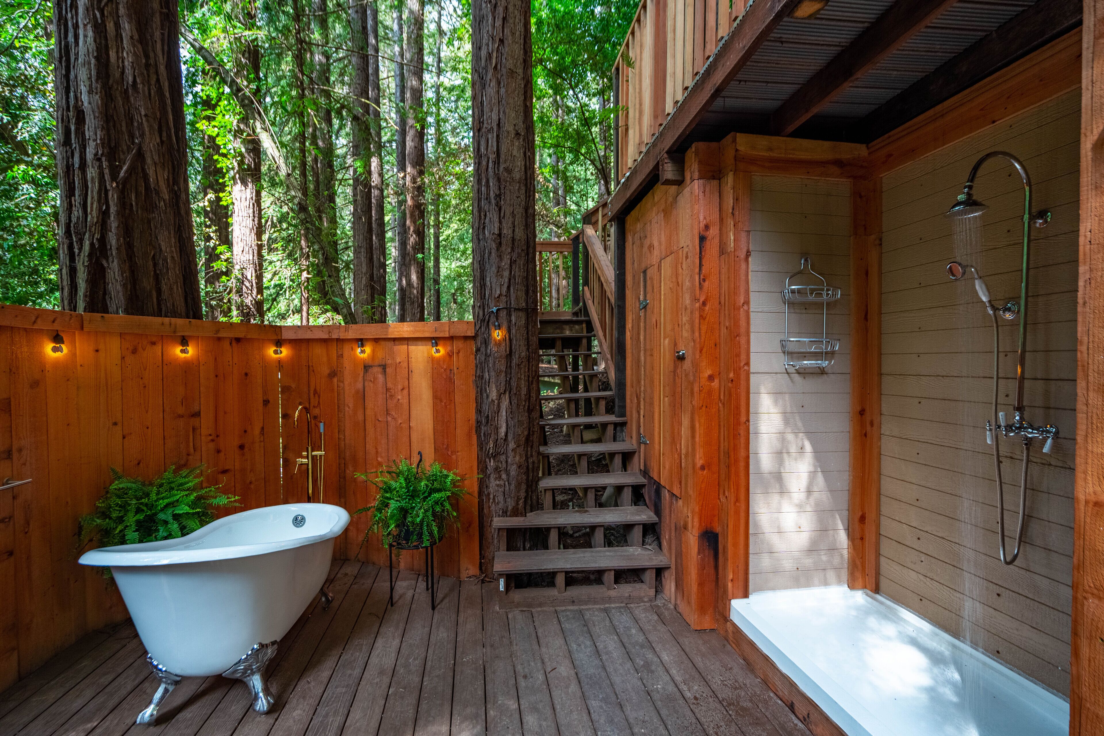 Une cabane en bois dotée d’une terrasse en bois, d’une baignoire sur pieds et d’un espace douche.