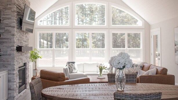 A spacious living room with a fireplace, large windows, and a high ceiling fan.
