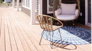 A wooden deck with a wicker chair and a patterned rug.