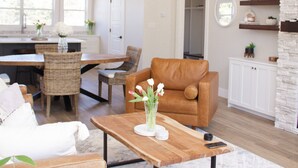 A spacious living area with a wooden coffee table, leather sofa, and dining area with wicker chairs.