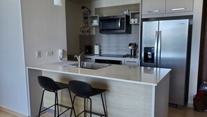 A modern kitchen with a central island, stainless steel appliances, and black bar stools. - OCEAN VIEW APARTMENT on the beach (Nueva Gorgona)