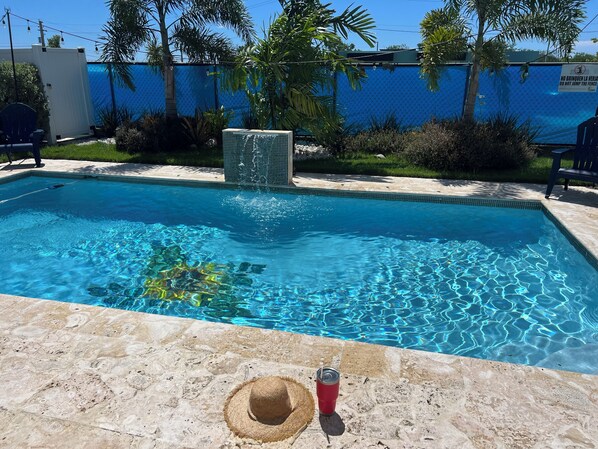 Una piscina con agua azul cristalina, un suelo de piedra y una bebida roja en el borde.