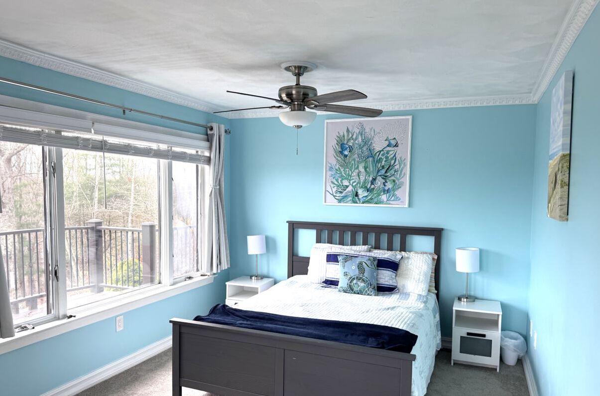 A bedroom with a bed, a ceiling fan, a window with blinds, and a painting on the wall.