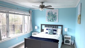 A bedroom with a bed, a ceiling fan, a window with blinds, and a painting on the wall. - Spacious House for Beach Getaway - Outdoor Shower -Beach Pass Included! (Charlestown)