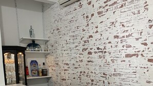 A kitchen with a white countertop, a wooden cabinet, and a brick wall. There are shelves with bottles and glasses. - Spacious House for Beach Getaway - Outdoor Shower -Beach Pass Included! (Charlestown)