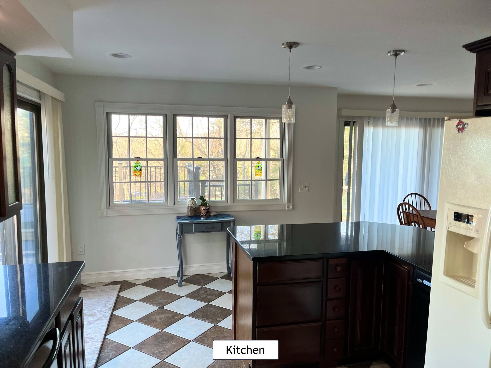 A kitchen with a checkered floor, a dining area with a table and chairs, and large windows with curtains.
